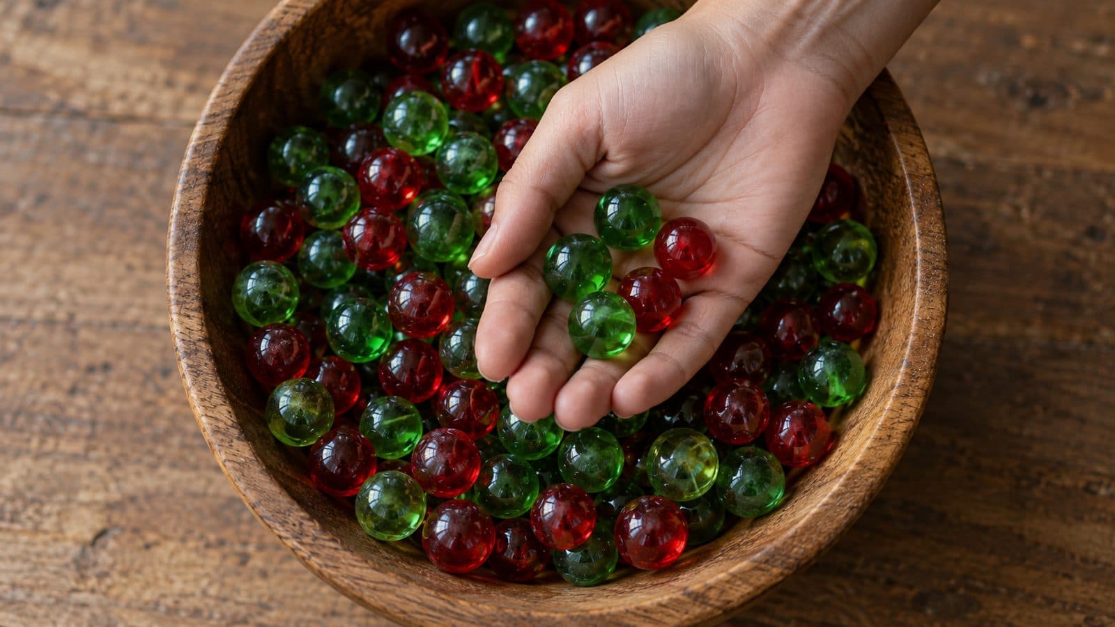 Hand holding more green than red marbles drawn from a mixed bowl, like a green-list bias in word choice.