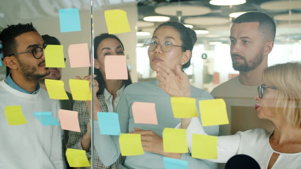 A marketing team collaborates around sticky notes on a glass board while planning a campaign