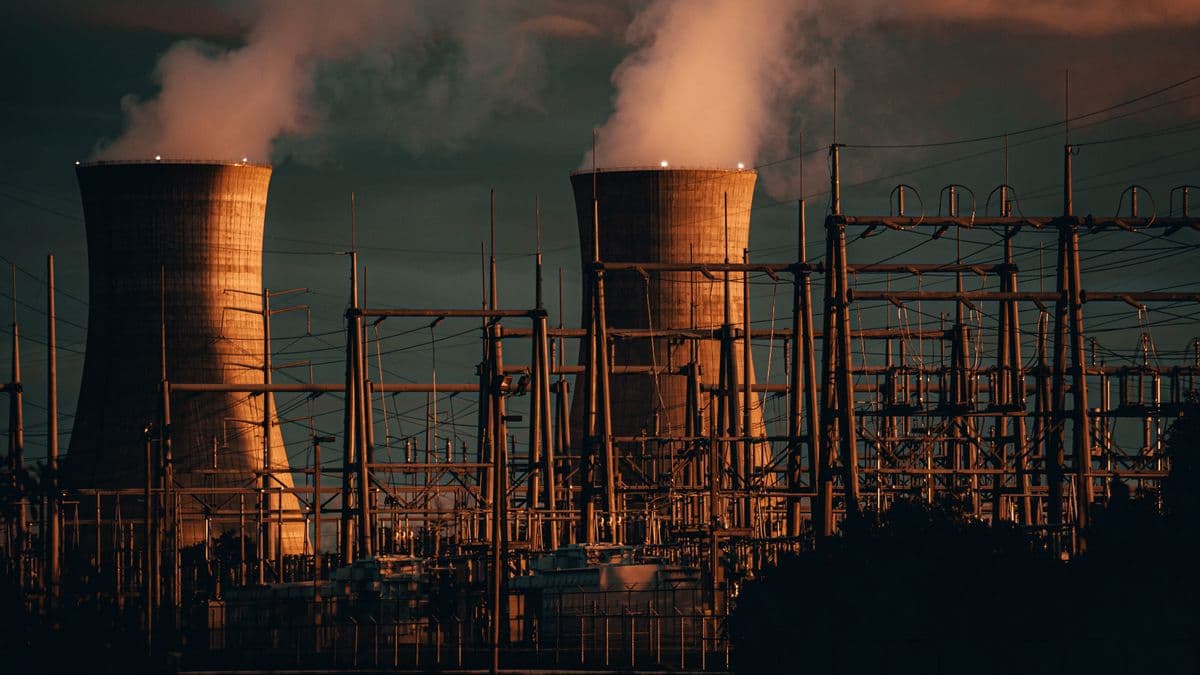 Two nuclear cooling towers venting steam at dusk behind a high-voltage substation, the energy side of the AI buildout that Gates's essay leaves unaddressed