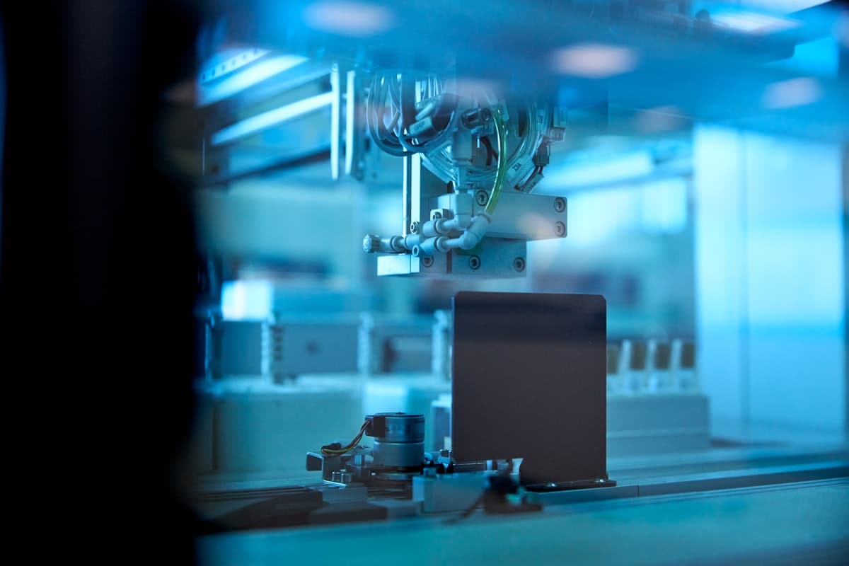 An industrial robotic arm performs precision handling tasks in a blue-lit automated factory floor