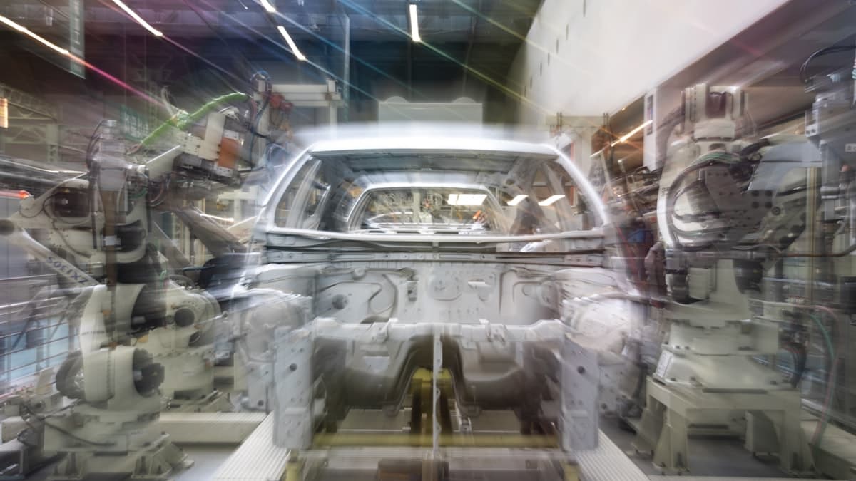 Multiple robotic arms perform coordinated assembly work on a car body along an automotive production line