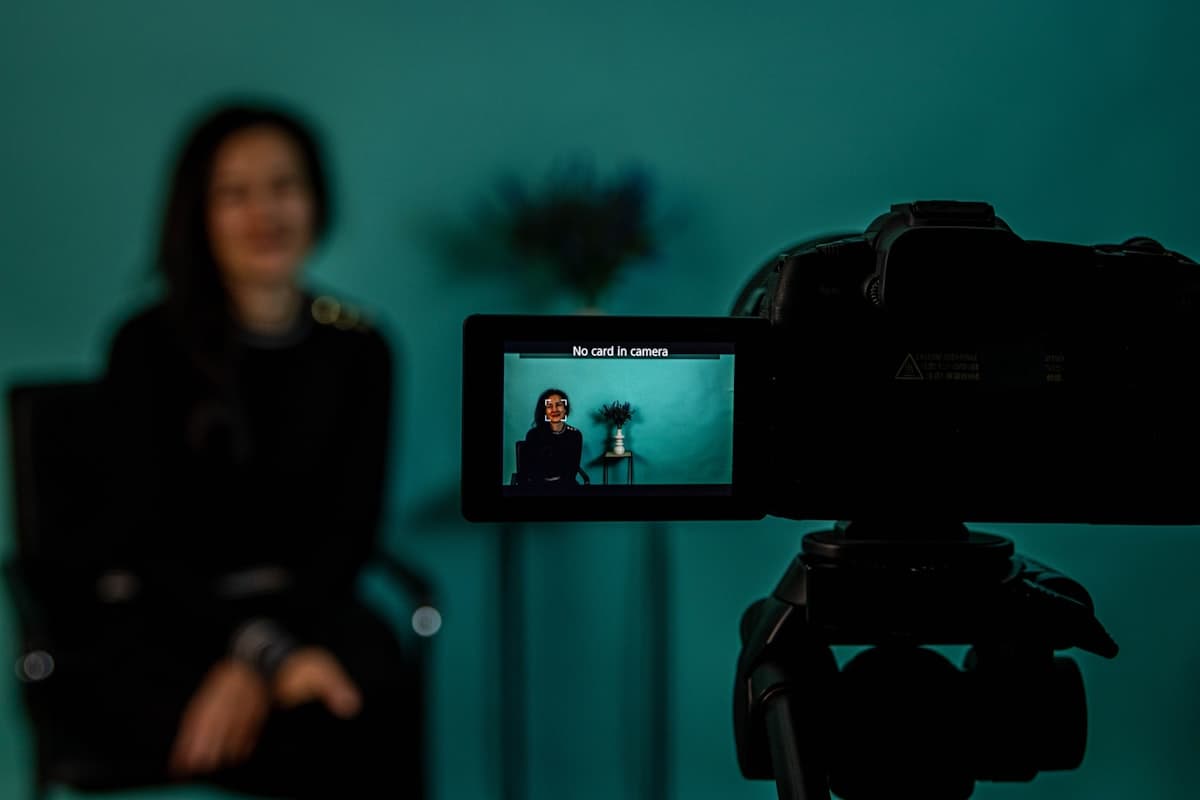 A content creator sits in front of a camera with its screen visible, framed for a filmed video segment