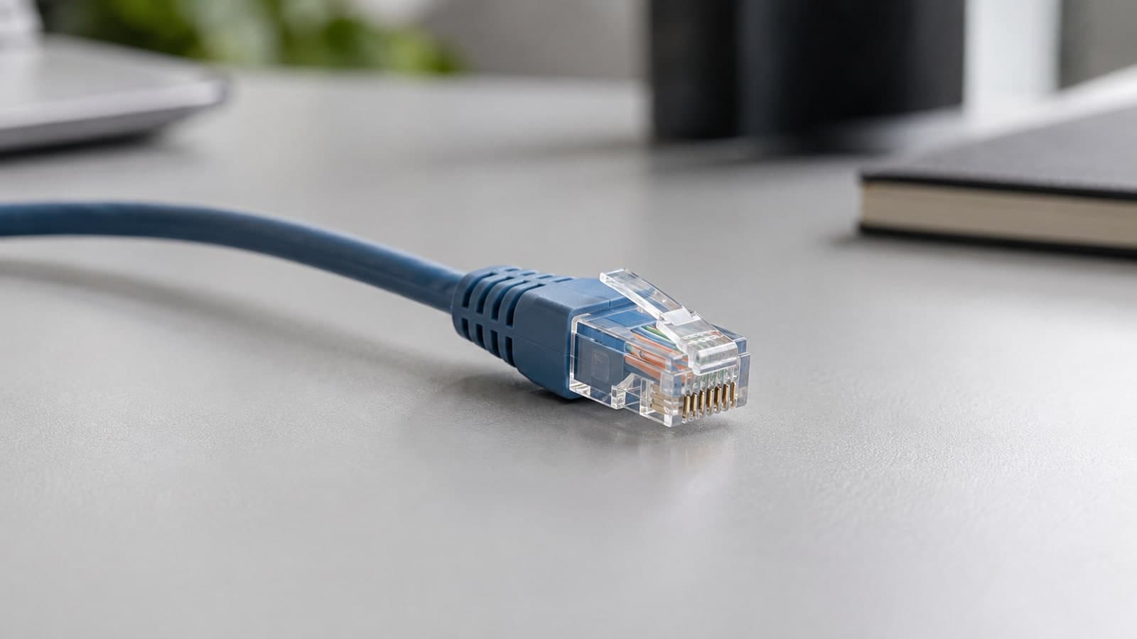 Close photograph of one muted blue Ethernet cable and its transparent connector on a light grey desk.