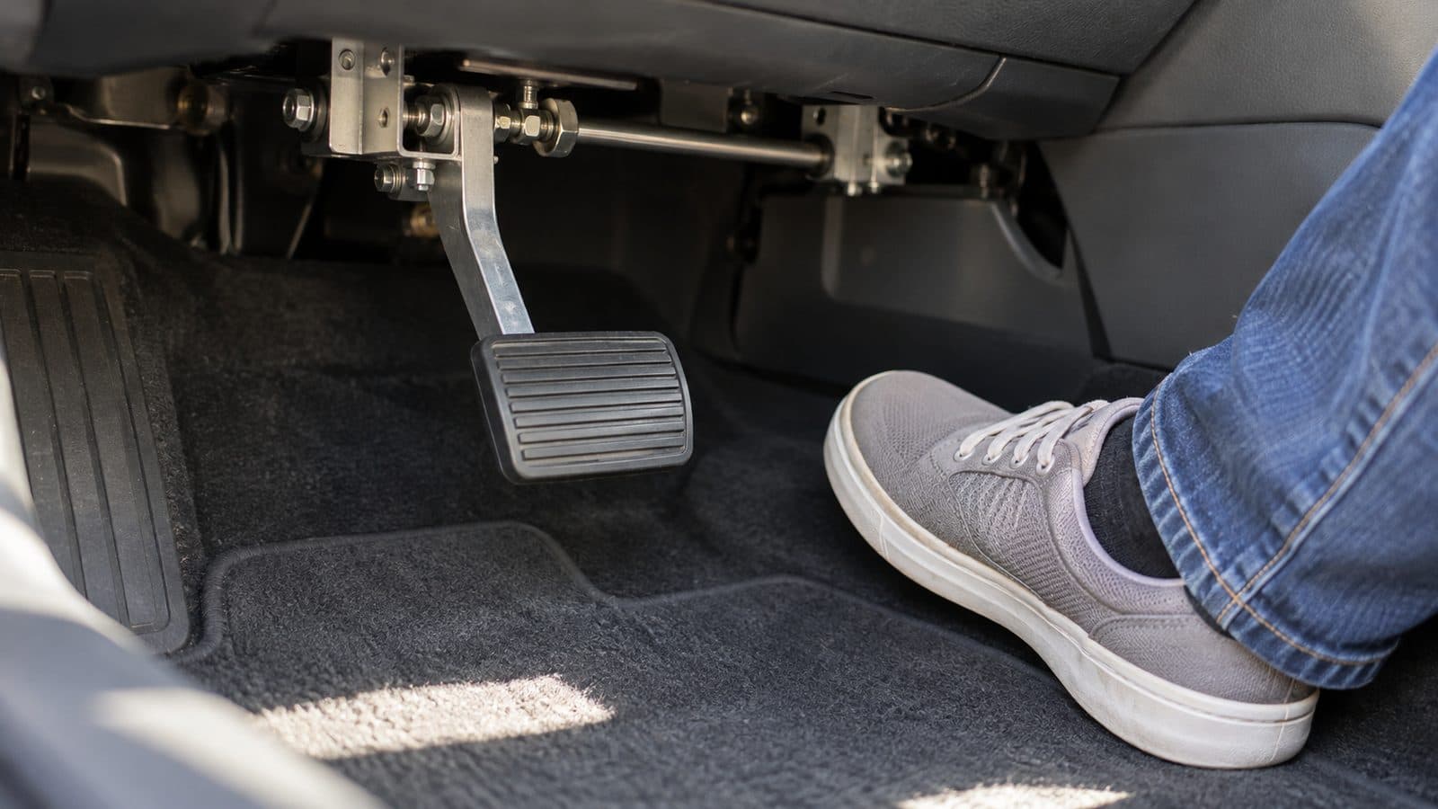 Second brake pedal on the passenger side of a driving-school car, a foot ready beside it, like an advertiser keeping watch over AI Max.